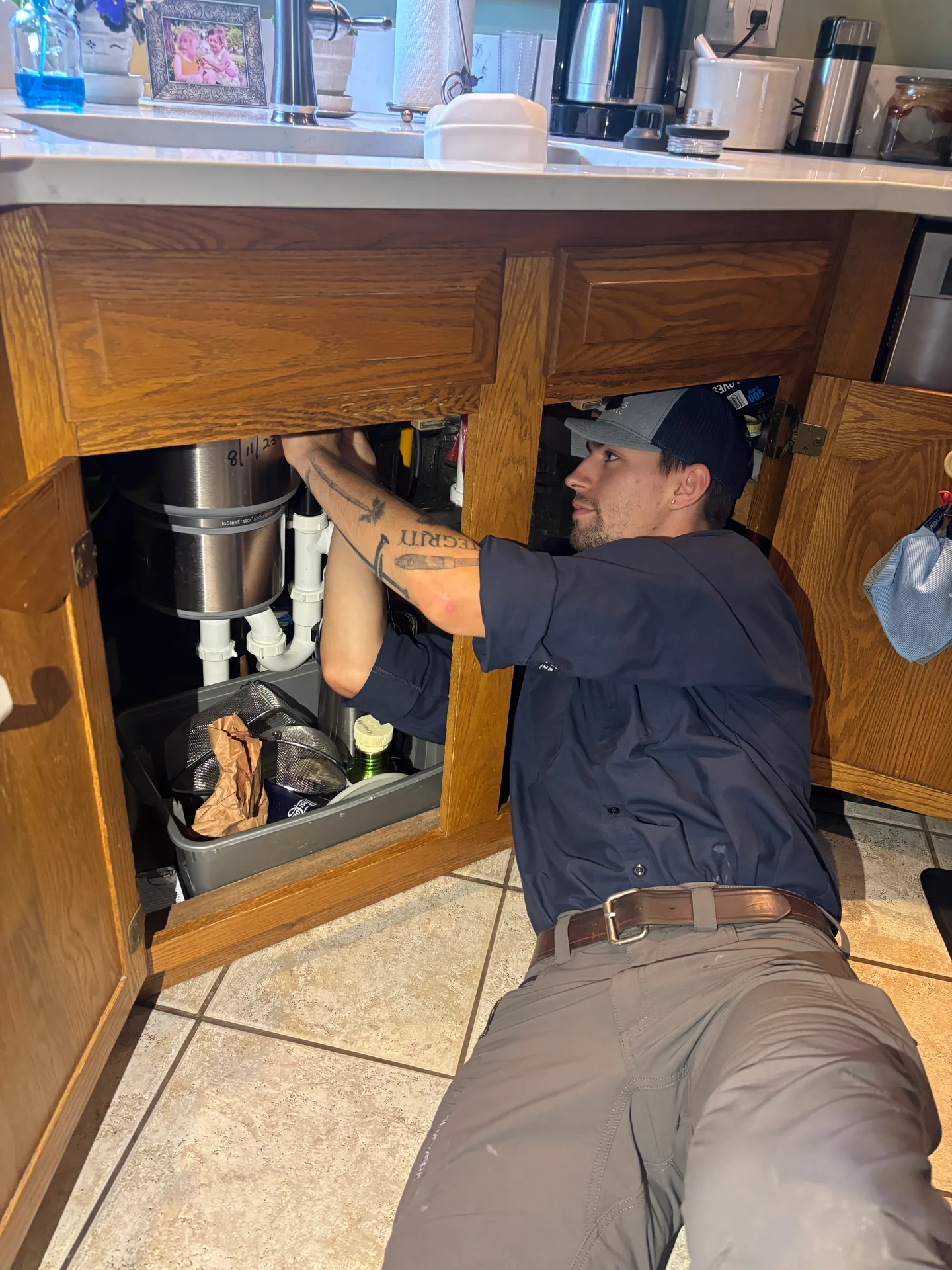 Garbage Disposal Service by Knauss Plumbing Knauss Plumbing owner servicing a garbage disposal and drain piping under a kitchen sink.