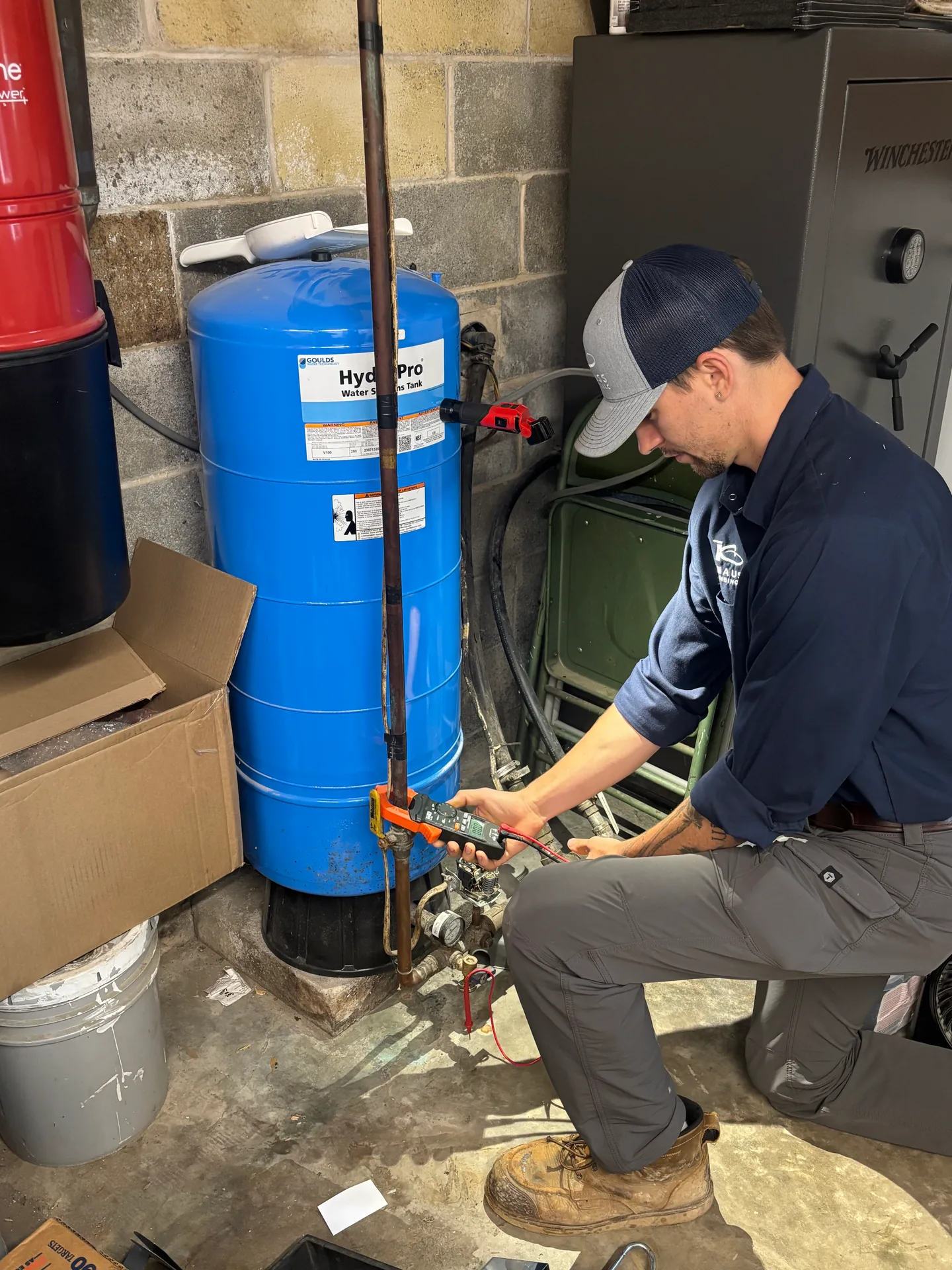Knauss Plumbing owner servicing a blue pressure tank in a home utility room.