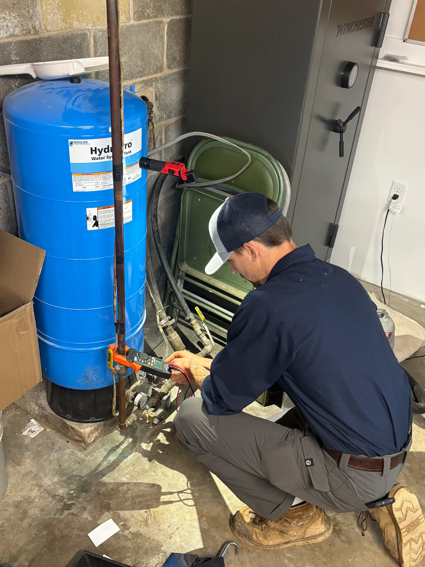 Knauss Plumbing owner repairing valves and piping beside a blue pressure tank.