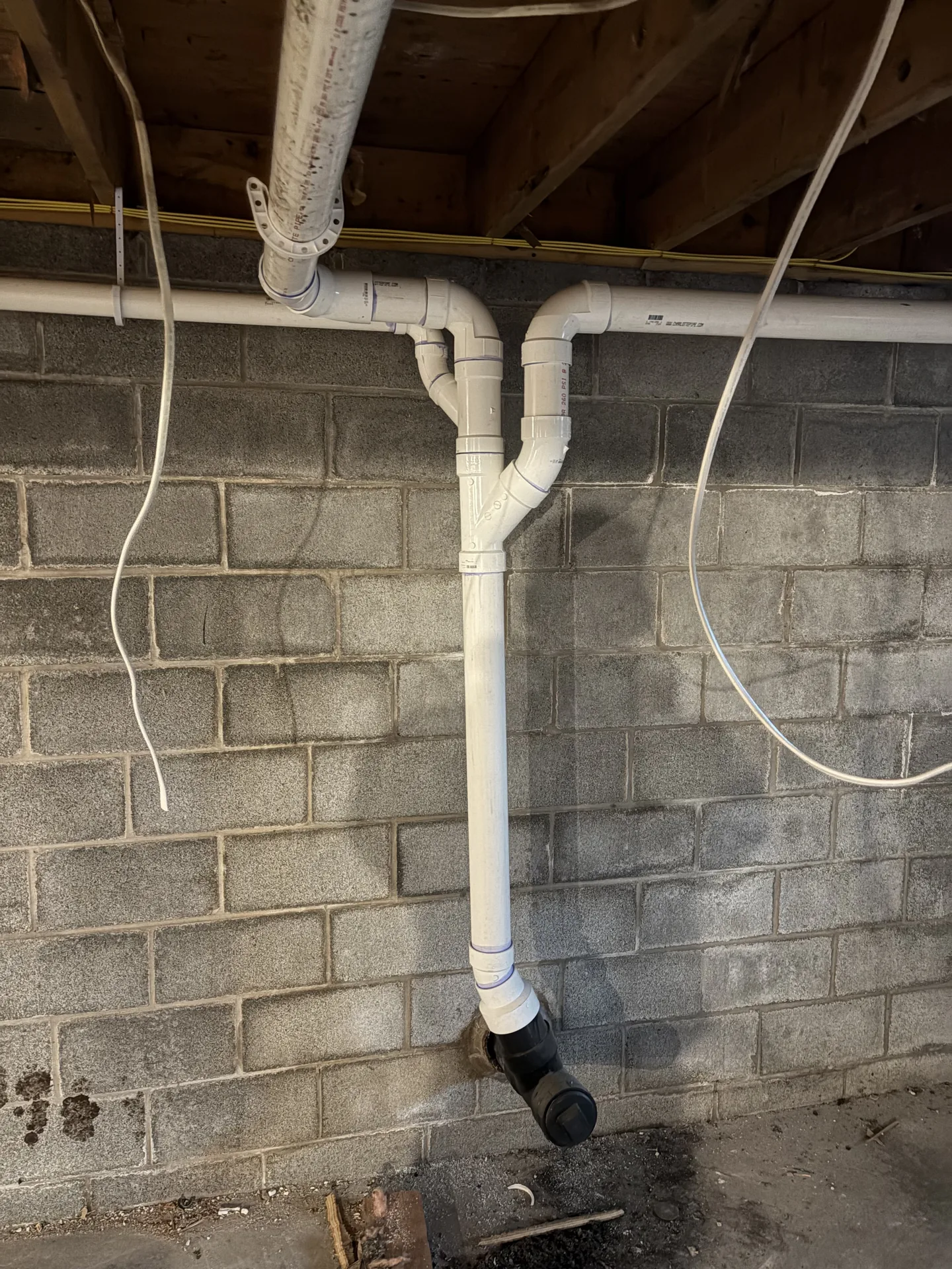 White PVC drain stack and fittings installed along a basement block wall.