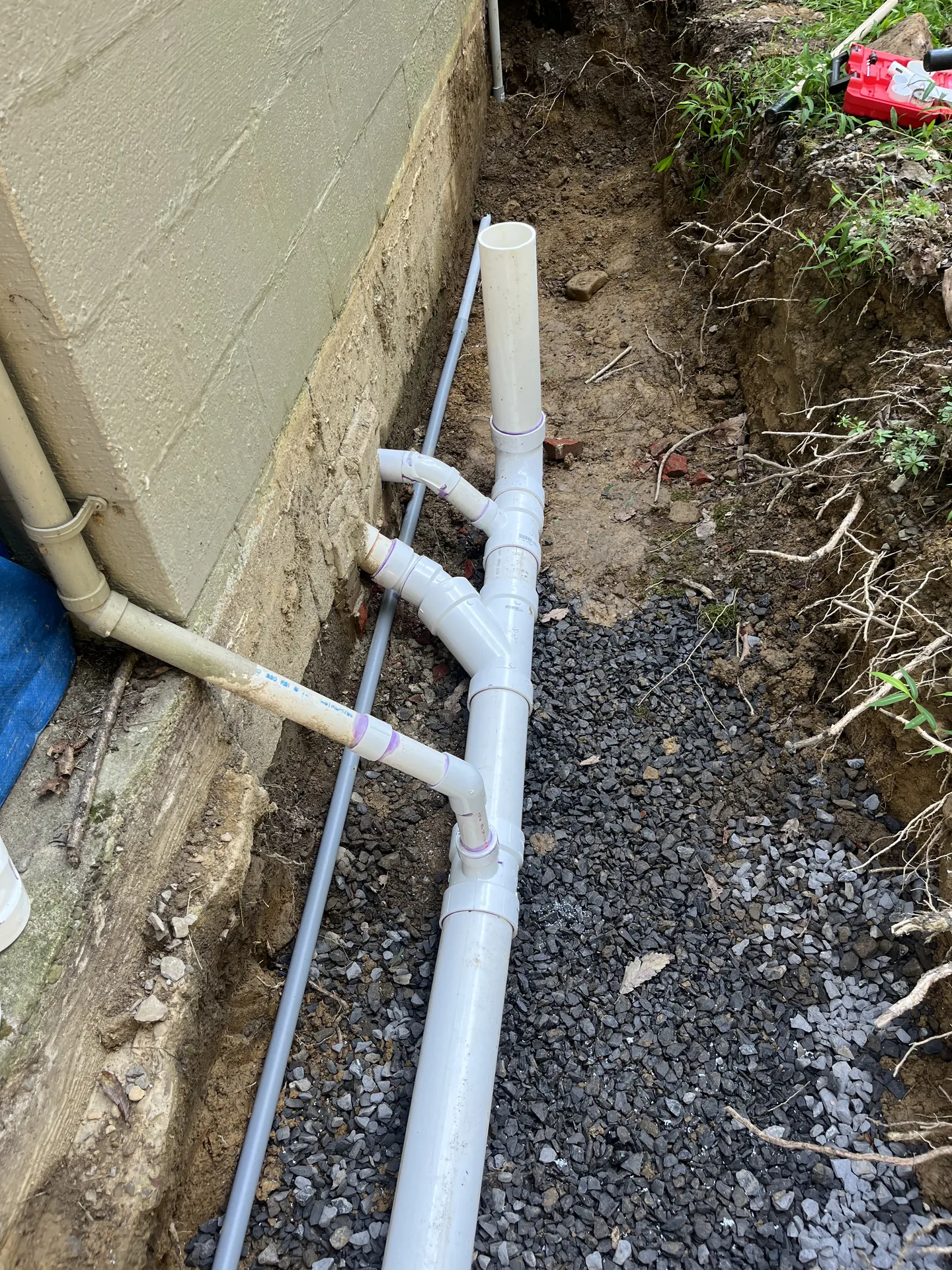 White PVC drain piping installed in an exterior trench beside a foundation wall.