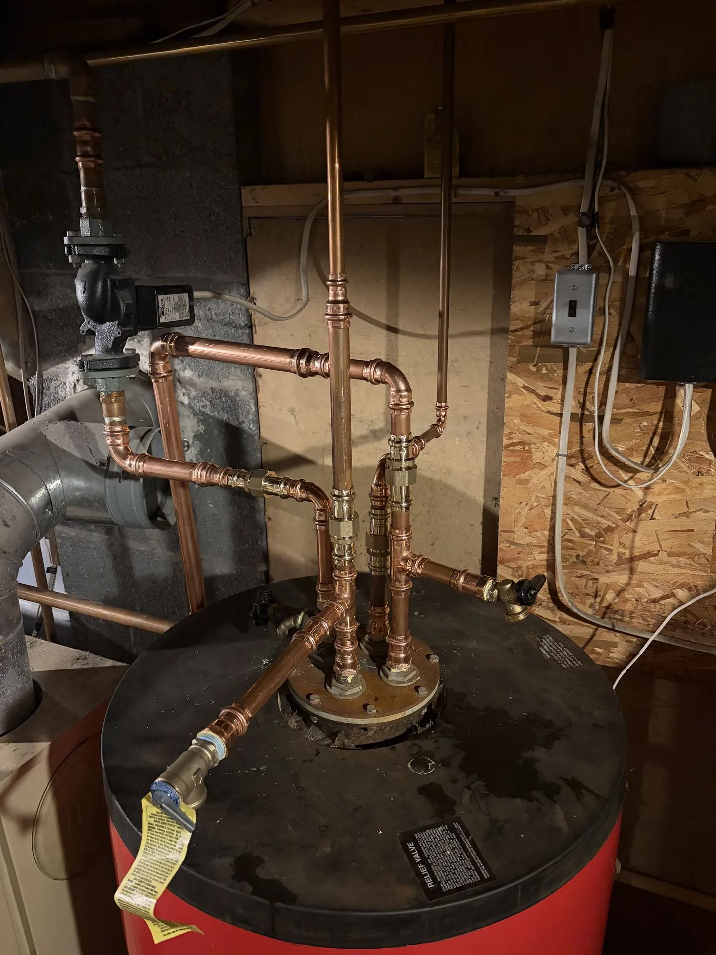 Water heater connected with clean copper piping in a basement mechanical area.
